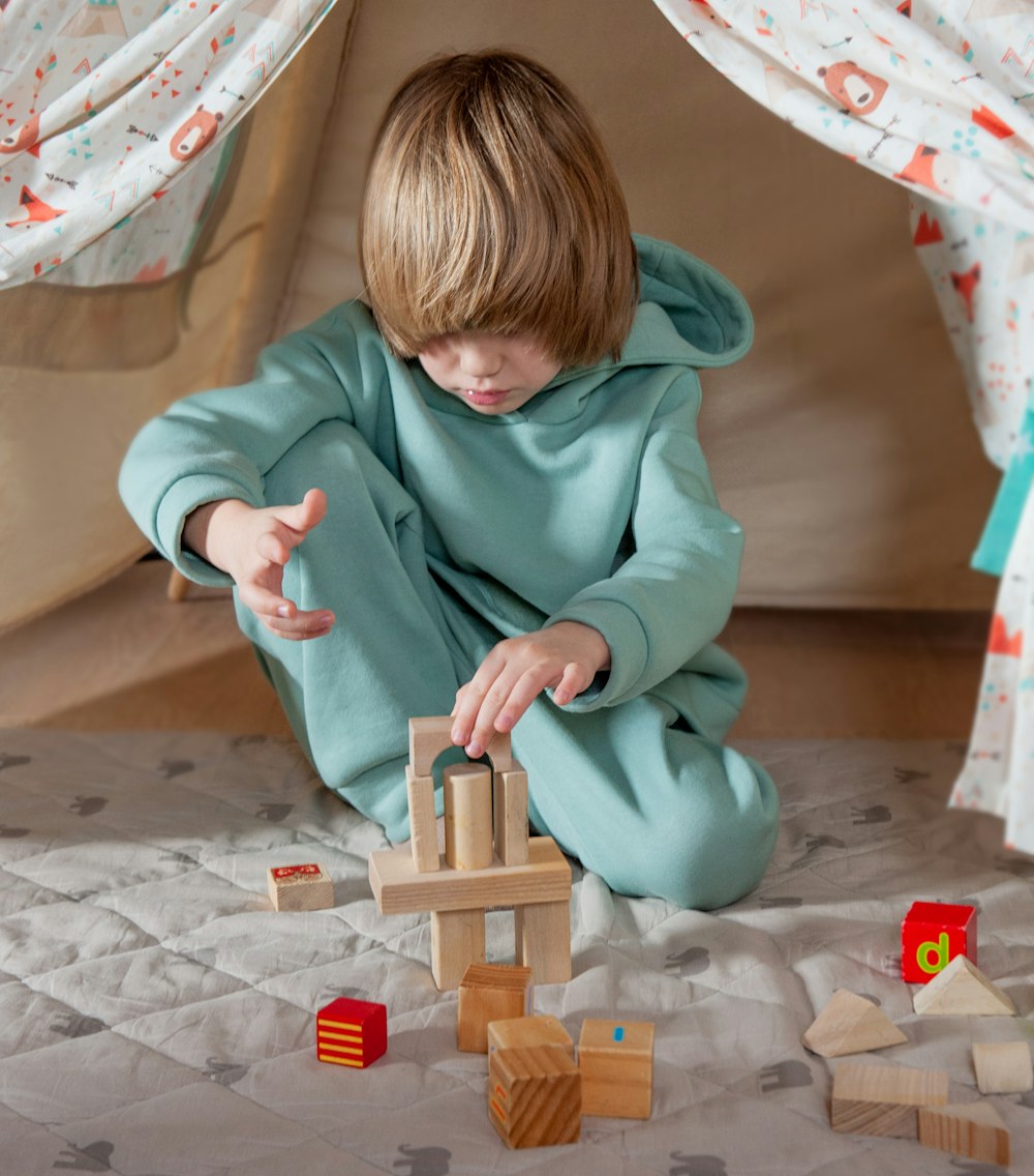 child in green hoodie playing with brown wooden blocks