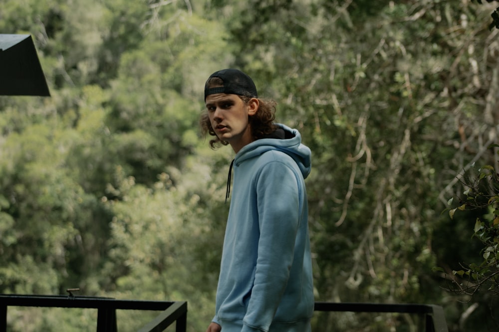 man in blue hoodie standing near green trees during daytime