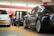 Several electric cars are charging in an indoor parking garage. The space is brightly lit with predominant red and white colors in the background. Charging cables are connected to the cars, highlighting a modern and technological atmosphere.