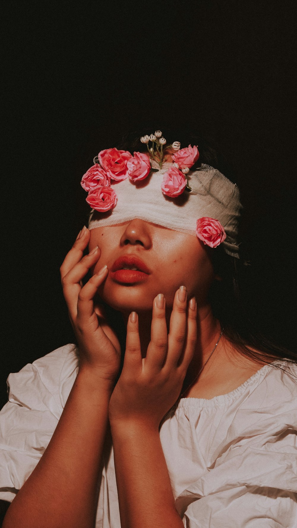 Femme en chemise blanche à col rond avec une fleur rouge sur son visage