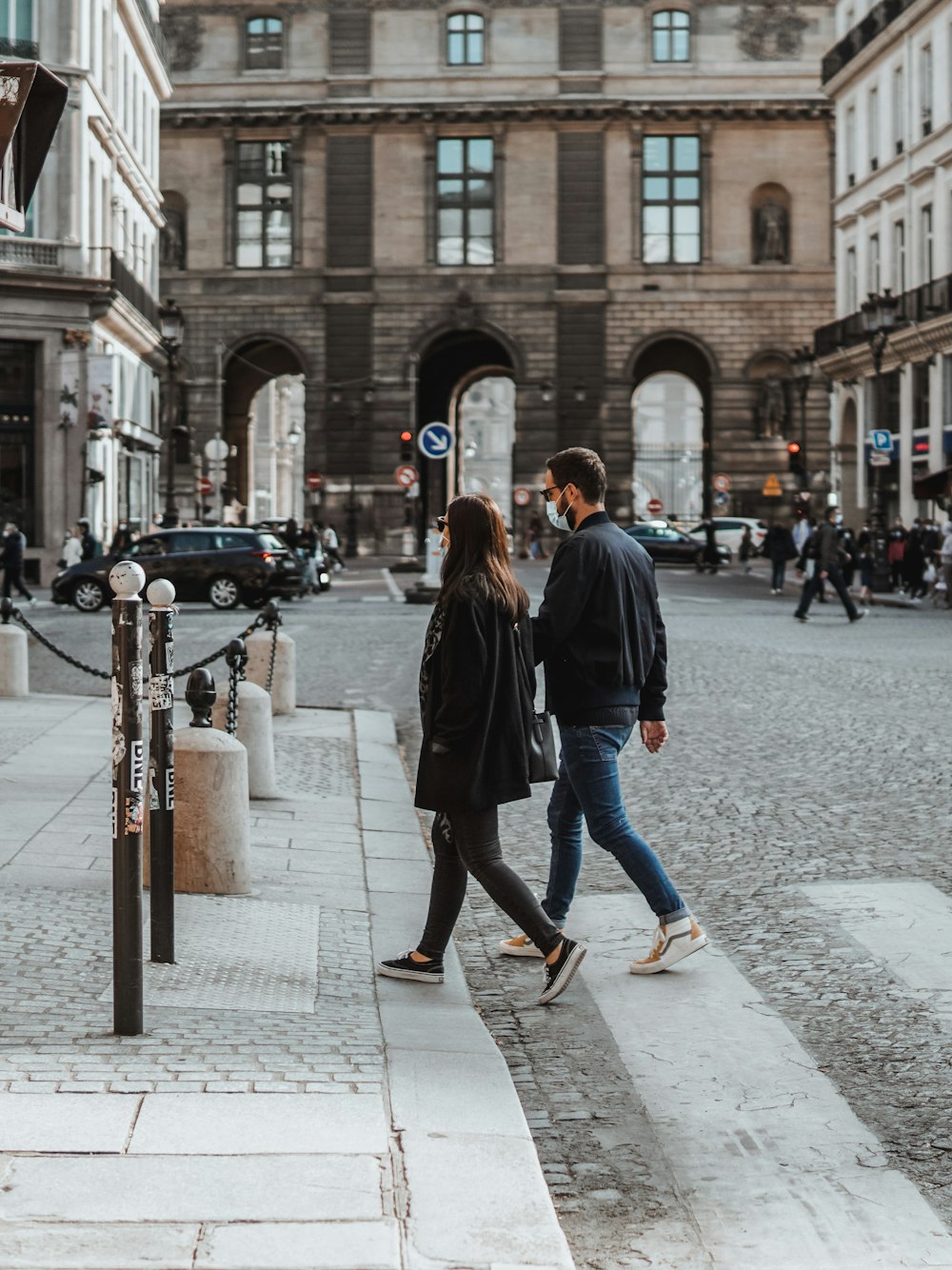 Femme en manteau noir et jean bleu debout sur le trottoir pendant la journée