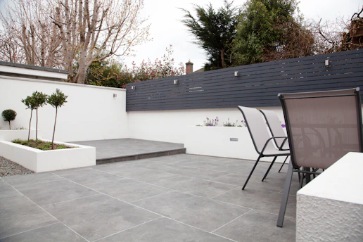 A sleek, modern outdoor living space with a deep royal purple accent wall, matte black railings, and soft grey stone flooring under soft silver lighting.