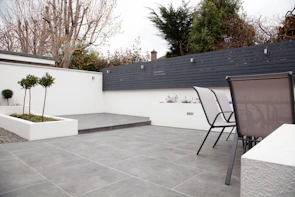 A modern patio area featuring stone tiles and lush green plants surrounding a cozy seating space.