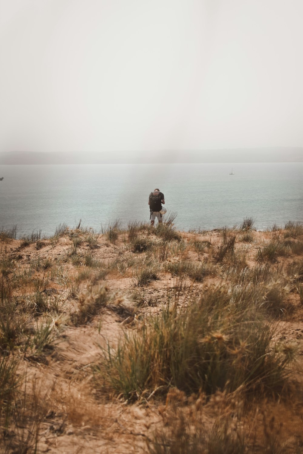 Person in schwarzer Jacke, die tagsüber auf einem braunen Grasfeld in der Nähe von Gewässern steht