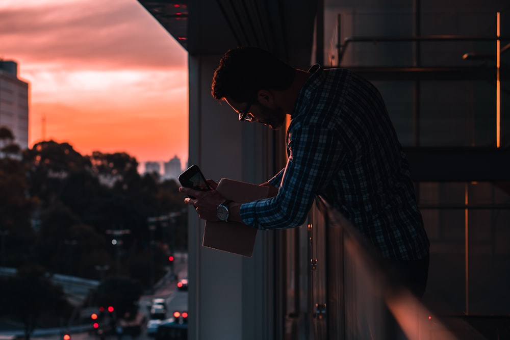 man in blue and white plaid dress shirt holding black smartphone