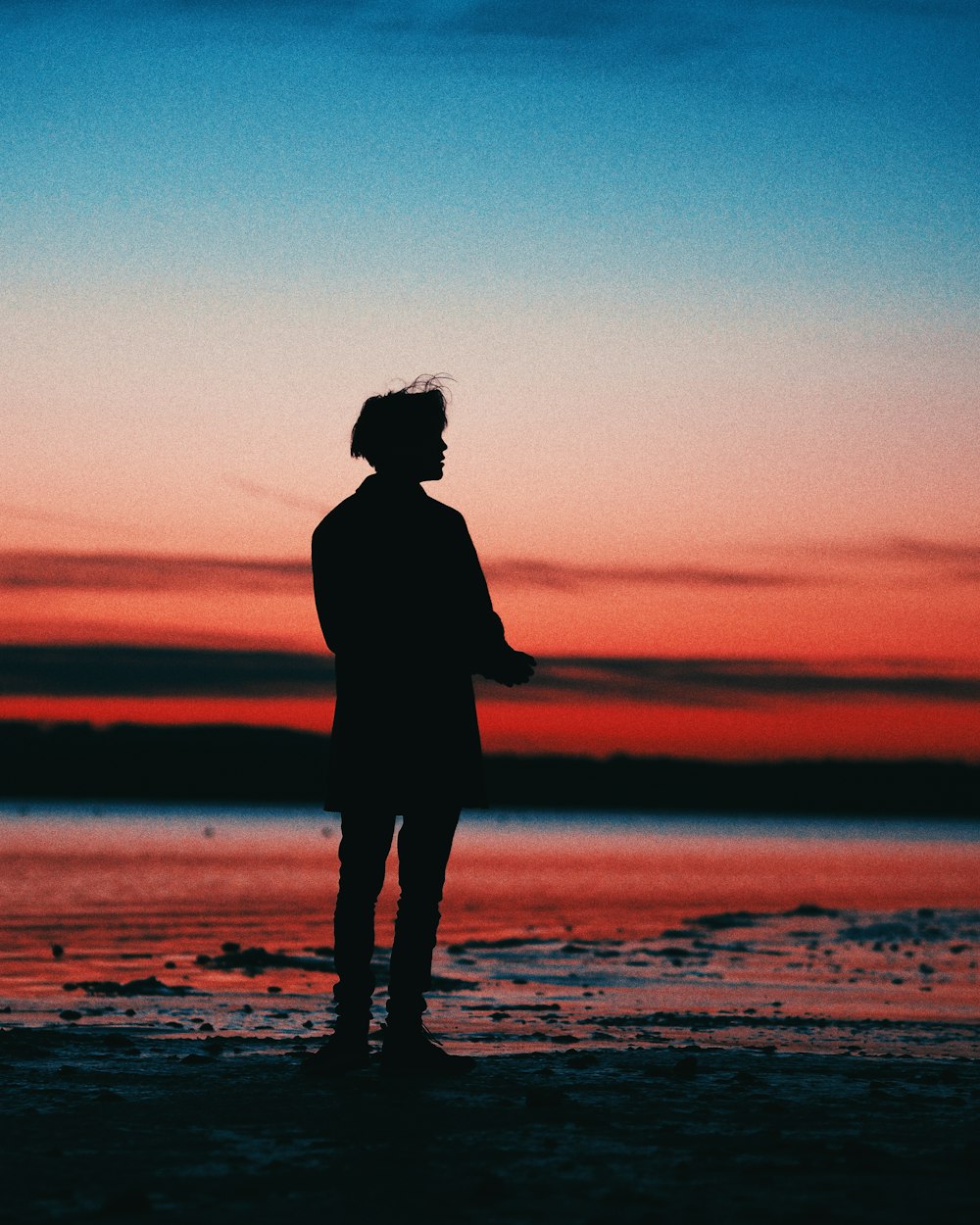 silhouette of woman standing on beach during sunset