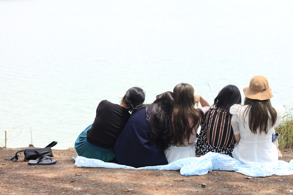 3 women sitting on brown sand near body of water during daytime