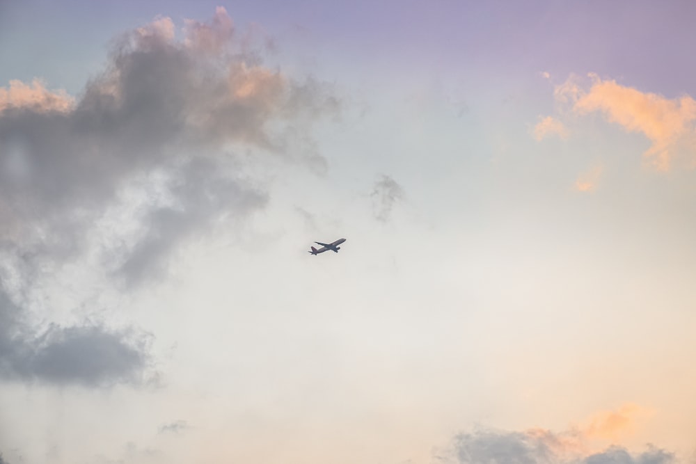 black airplane flying under white clouds during daytime