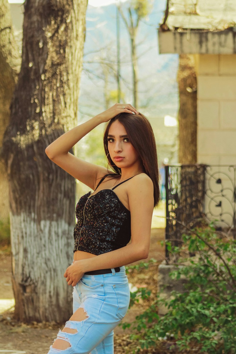 woman in black spaghetti strap top and blue denim shorts standing beside brown tree during daytime