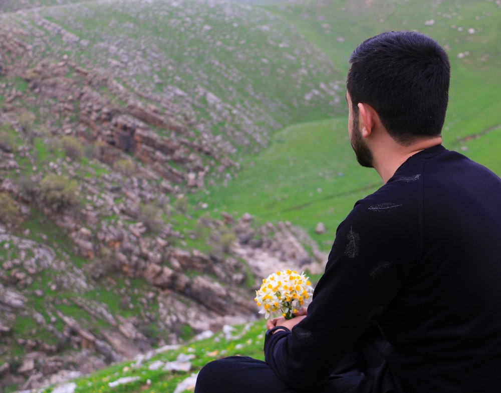 man in black suit jacket sitting on rock looking at the mountains during daytime