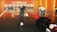 People are enjoying a game of bowling in a modern alley. The space is warmly lit with orange tones and features multiple lanes, each with an overhead screen displaying scores. Bowling balls are visible, including an eight ball being held by a player ready to roll. Another player is setting up his turn, and there are people in the background, focusing on their games.