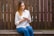 woman in white long sleeve shirt and blue denim jeans sitting on brown wooden bench