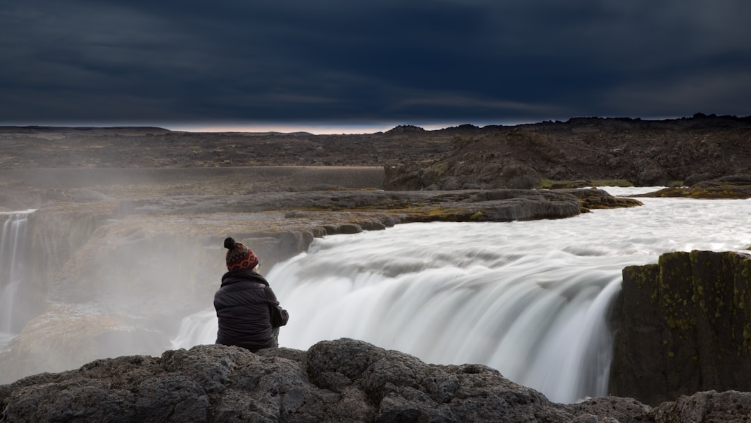 man in red jacket sitting on rock near waterfalls during daytime