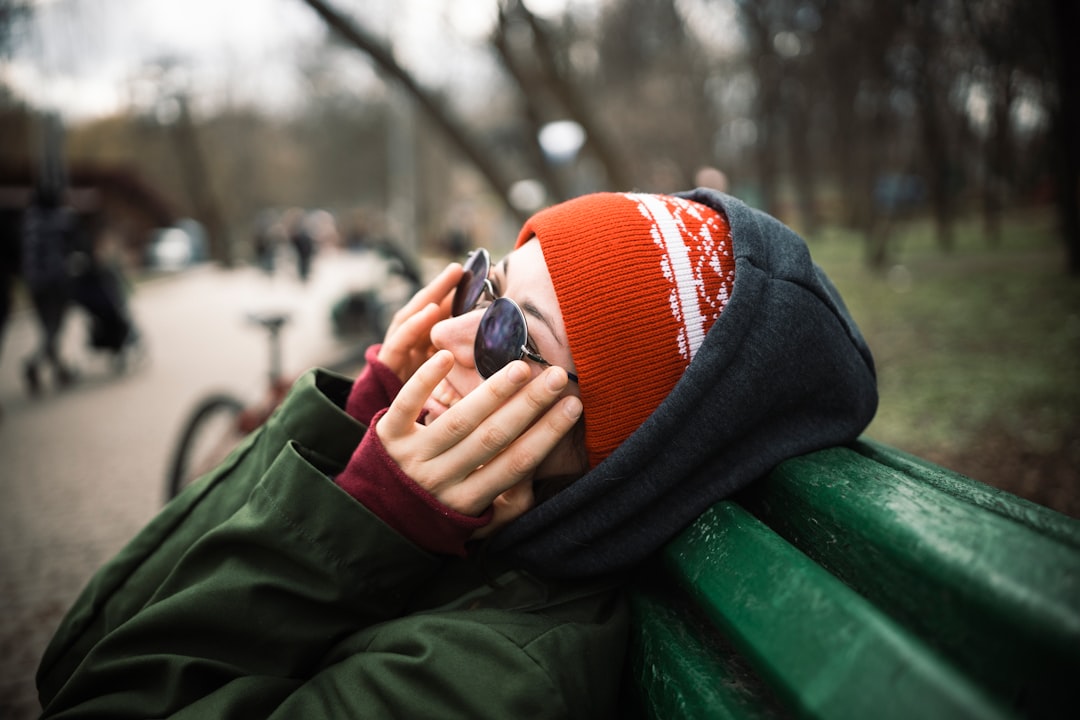 person in red and white knit cap and green jacket sitting on green bench during daytime