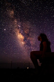 woman in black tank top and black pants sitting on brown wooden bench during night time
