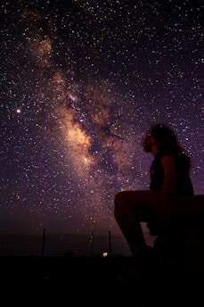 woman in black tank top and black pants sitting on brown wooden bench during night time