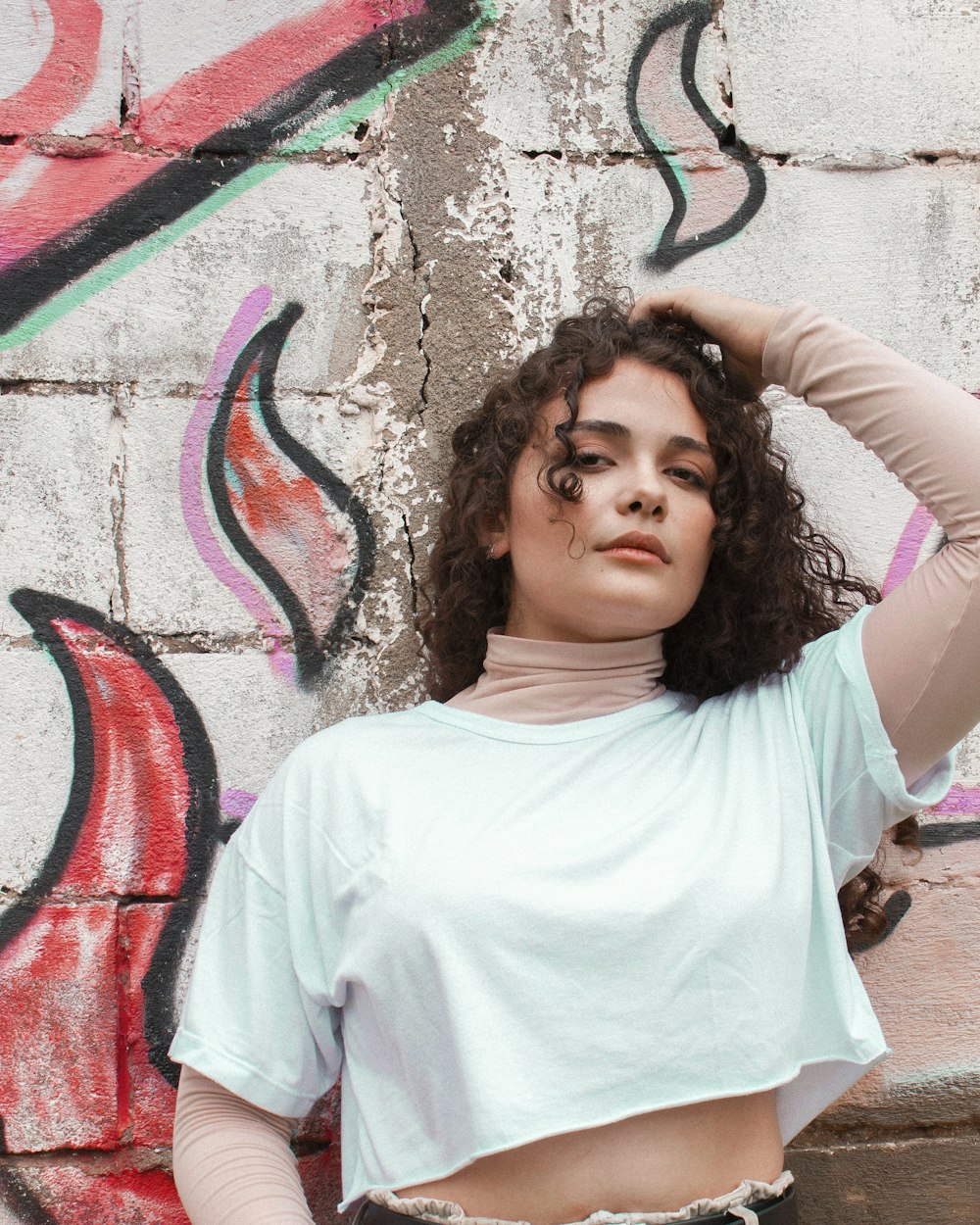 girl in white crew neck t-shirt standing near wall with graffiti during daytime