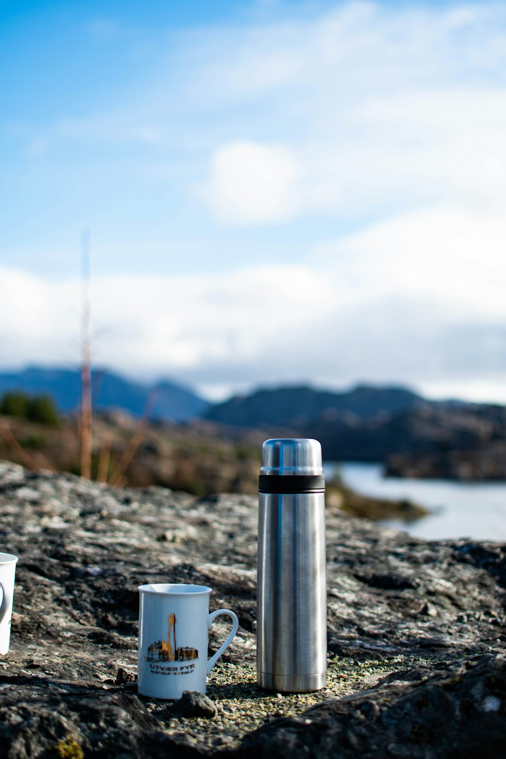 Tasse en céramique blanche sur roche grise près du plan d’eau pendant la journée