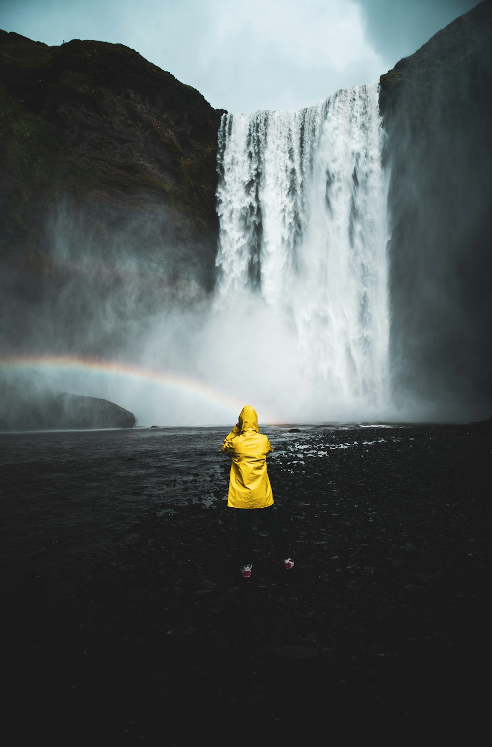 person in yellow hoodie standing in front of waterfalls