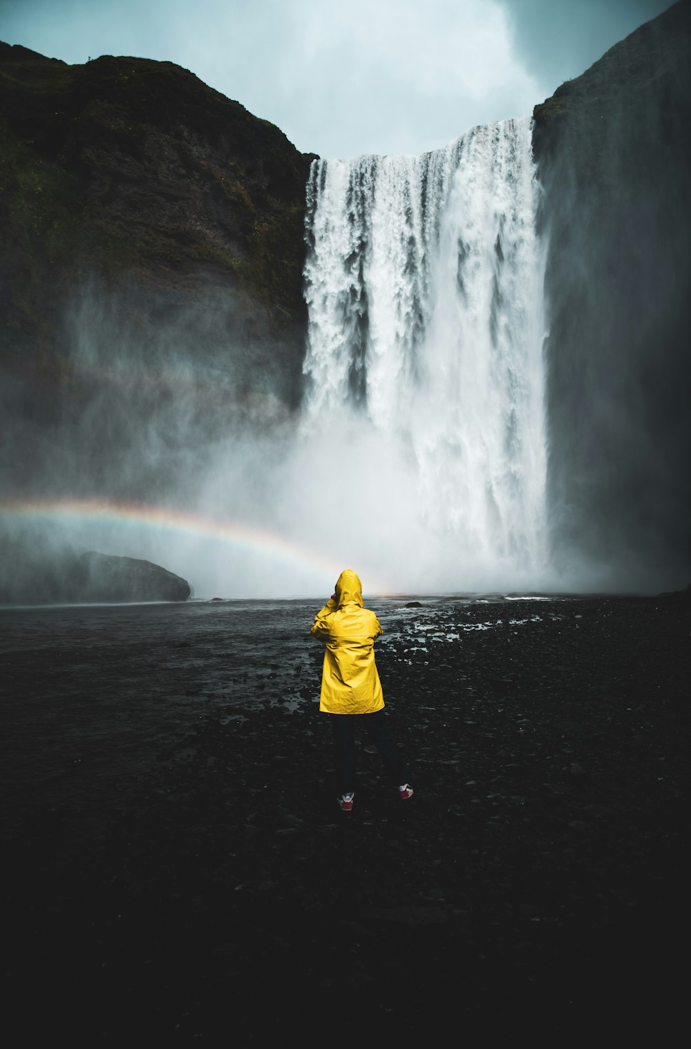 Persona con sudadera con capucha amarilla de pie frente a cascadas