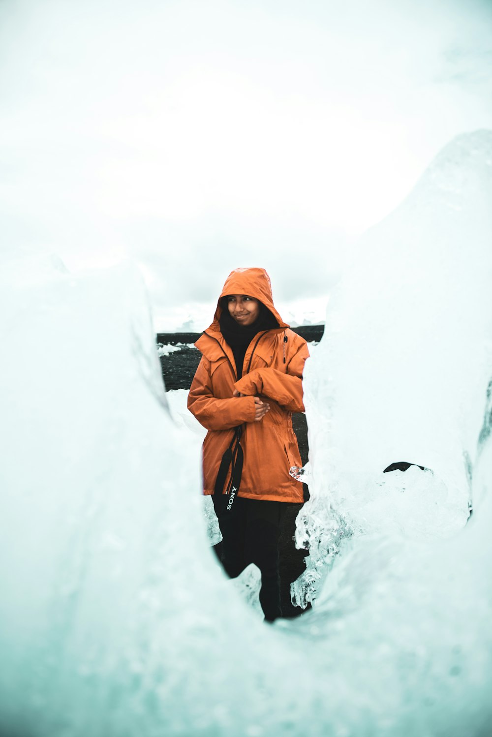 woman in orange hoodie standing on snow covered ground during daytime