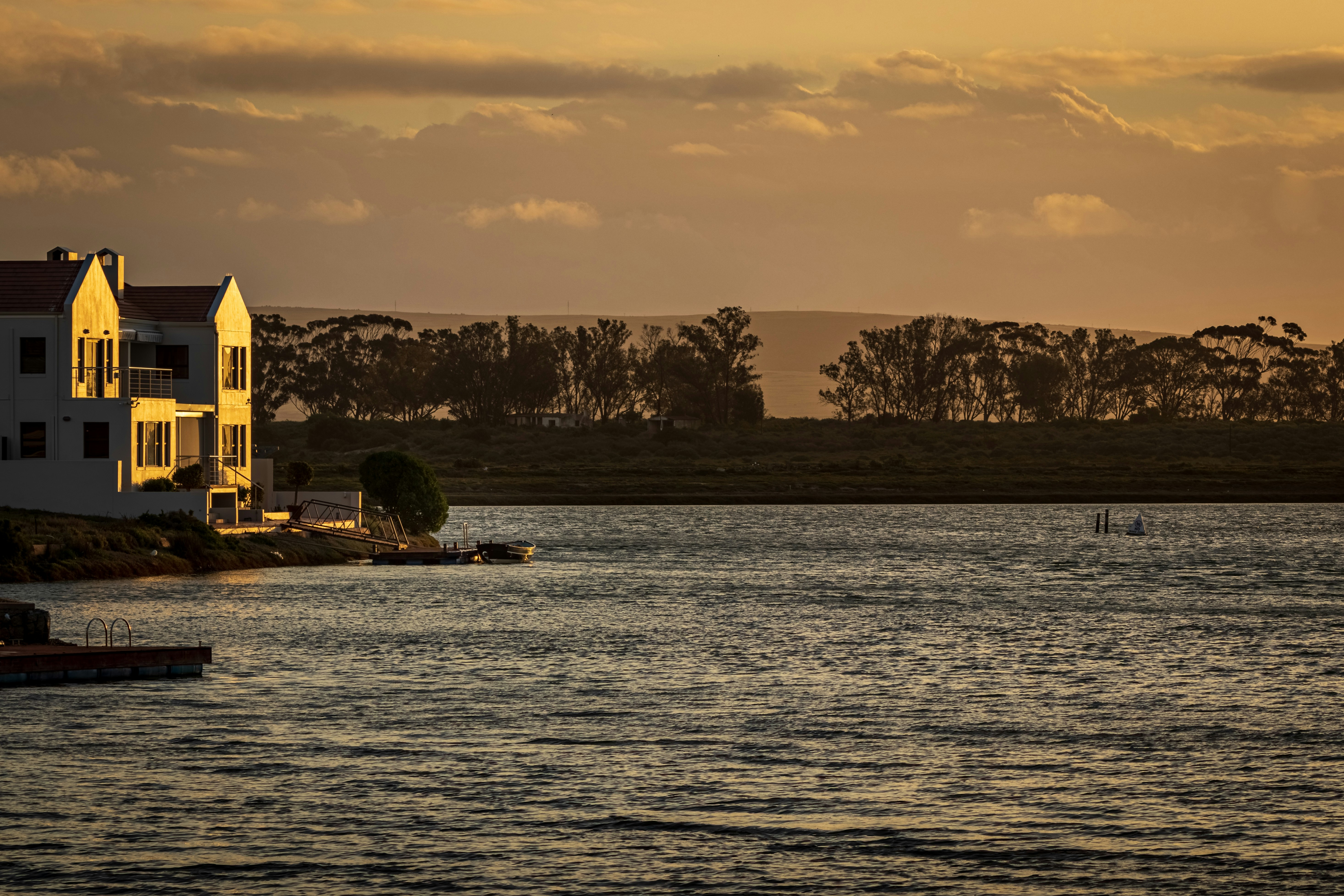 Holiday home on marina at sunset with a silhouette of trees in the background and clouds in the sky. 
