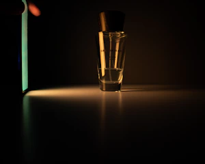 Close-up of a sleek perfume bottle with a soft glow highlighting its elegant curves against a dark background.