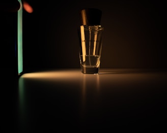 A moody, cinematic close-up of a sleek perfume bottle resting on a dark velvet surface with soft golden light highlighting its contours.