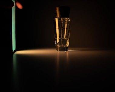 Close-up of a perfume bottle releasing a delicate fragrance cloud in low light.