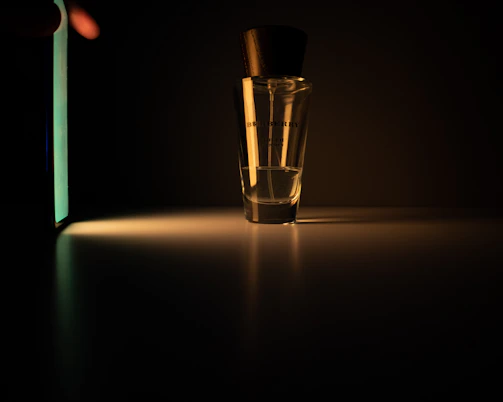 A sleek, metallic perfume bottle illuminated by dramatic golden light against a deep black background.