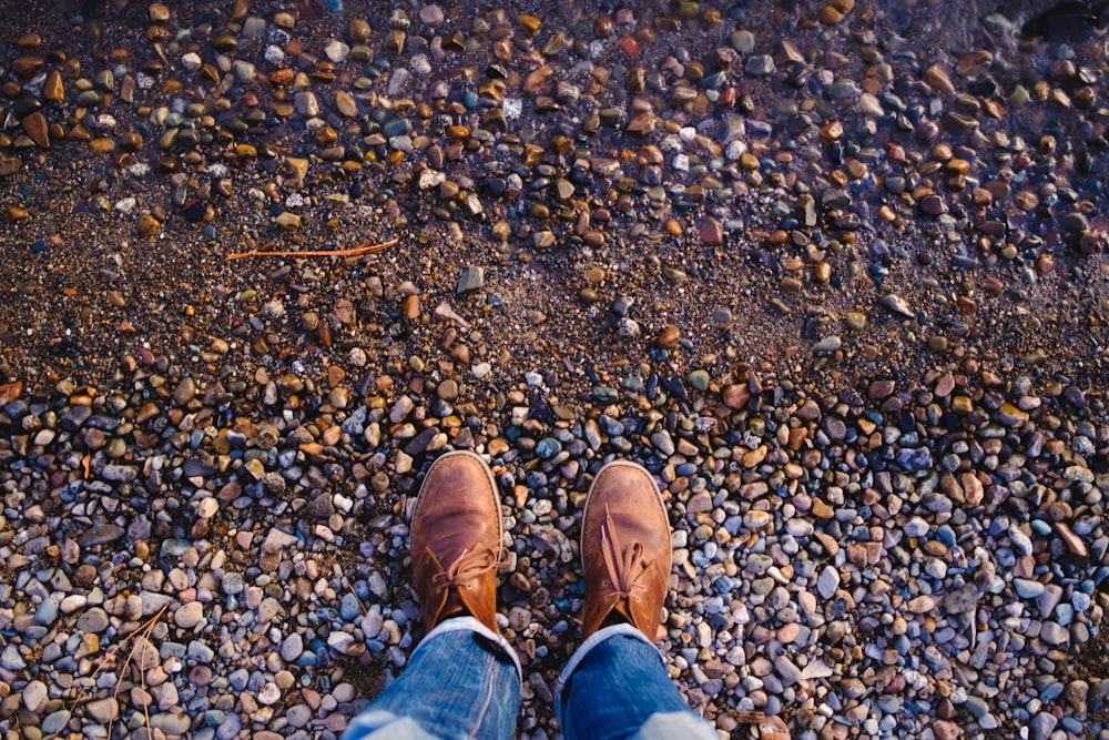 Persona in jeans blu denim e scarpe di pelle marrone in piedi su terreno roccioso