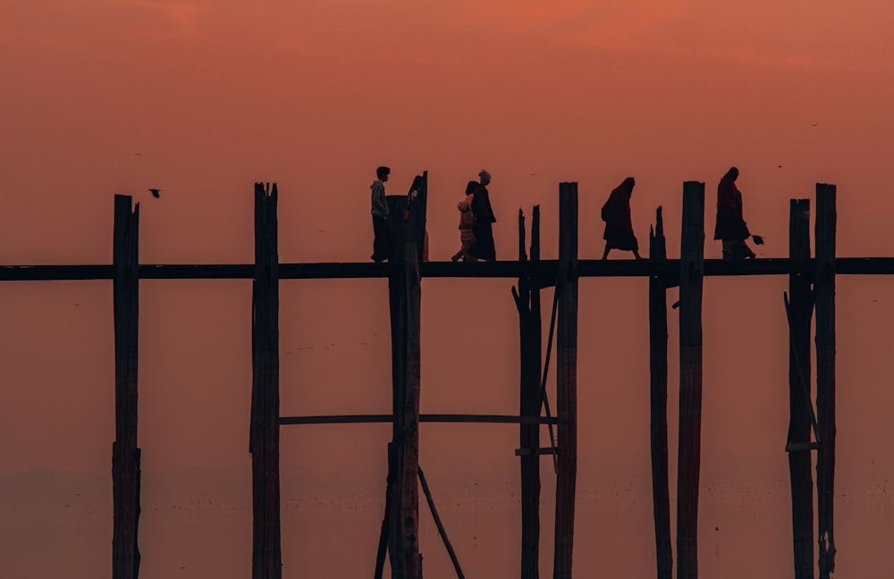 silhouette of people standing on wooden fence during sunset