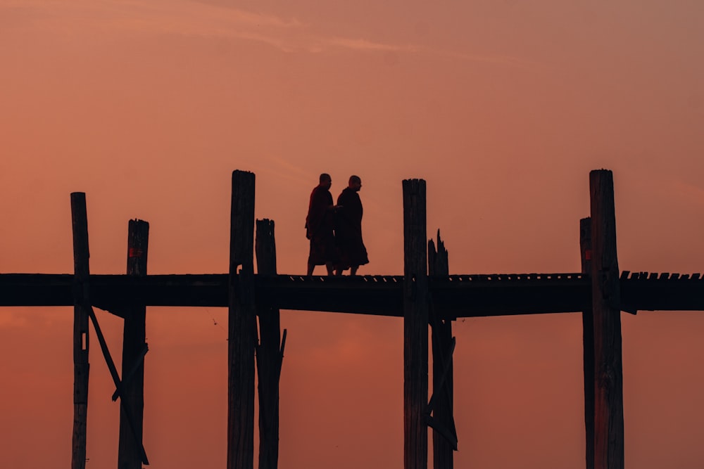 silhouette of man and woman standing on wooden fence during sunset