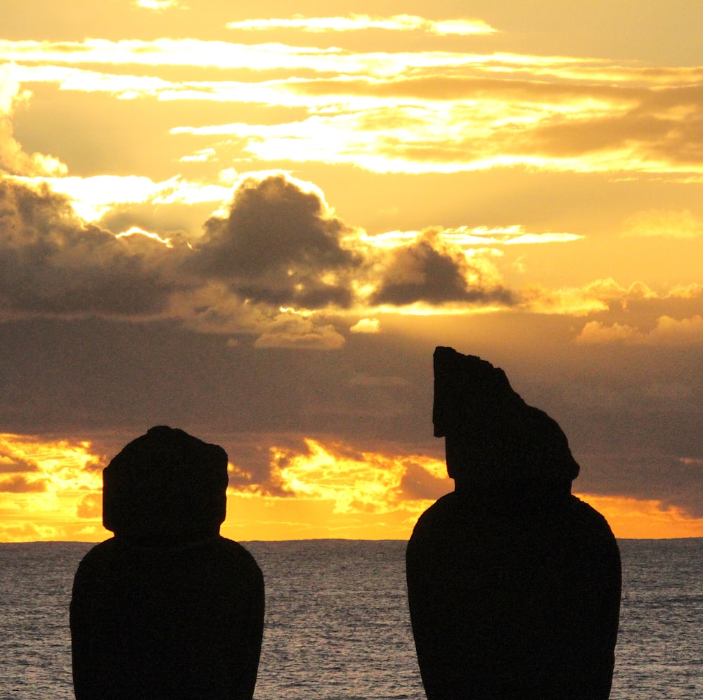 silhouette of two rock formation on body of water during sunset