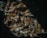 A pile of dried fish with a textured and rough appearance, featuring prominent eyes and scales. The fish are stacked closely together with a dark background, enhancing their metallic and earthy tones.