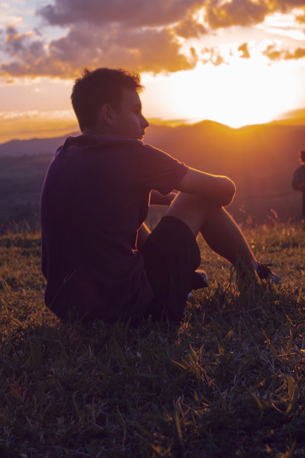 boy in black hoodie sitting on grass during sunset