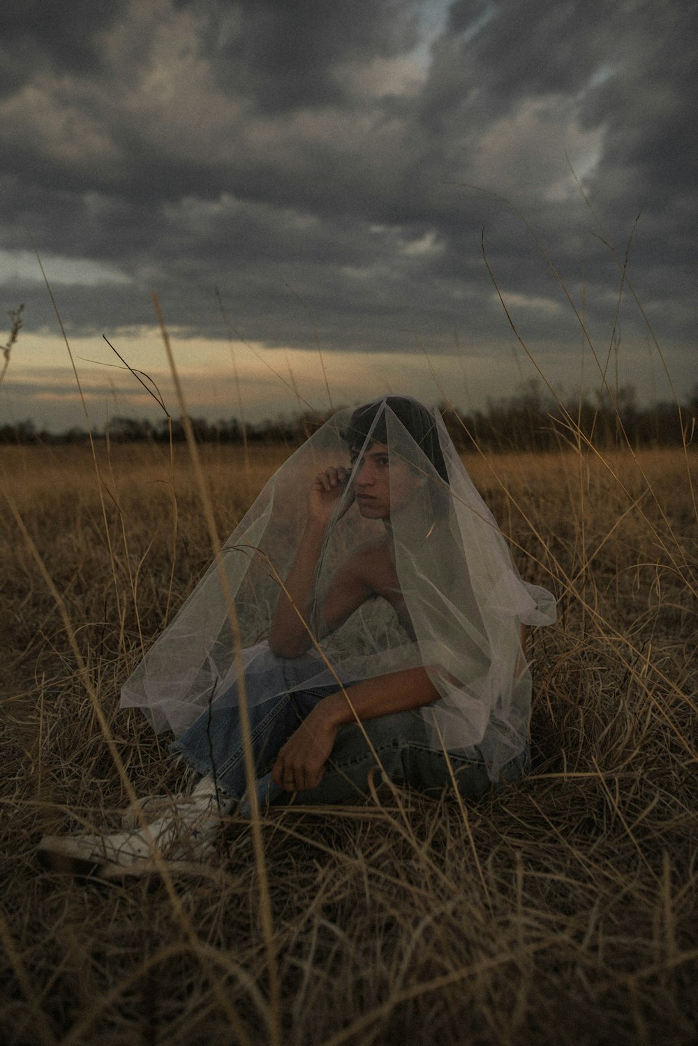 Femme en robe de mariée blanche assise sur le champ d’herbe brune pendant la journée