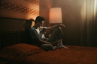 A softly lit bedroom with textured linen bedding and a trendy woman reading a book barefoot on the bed.