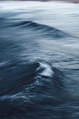 Dark blue ocean waves create a dynamic and fluid scene with light reflecting off the choppy surface, giving a sense of motion and depth.
