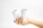 A hand holds two white aluminum cans against a plain white background. The cans are plain with no labels, and they are positioned upright with the opening tabs visible. The lighting is bright and even, emphasizing the minimalist aesthetic.