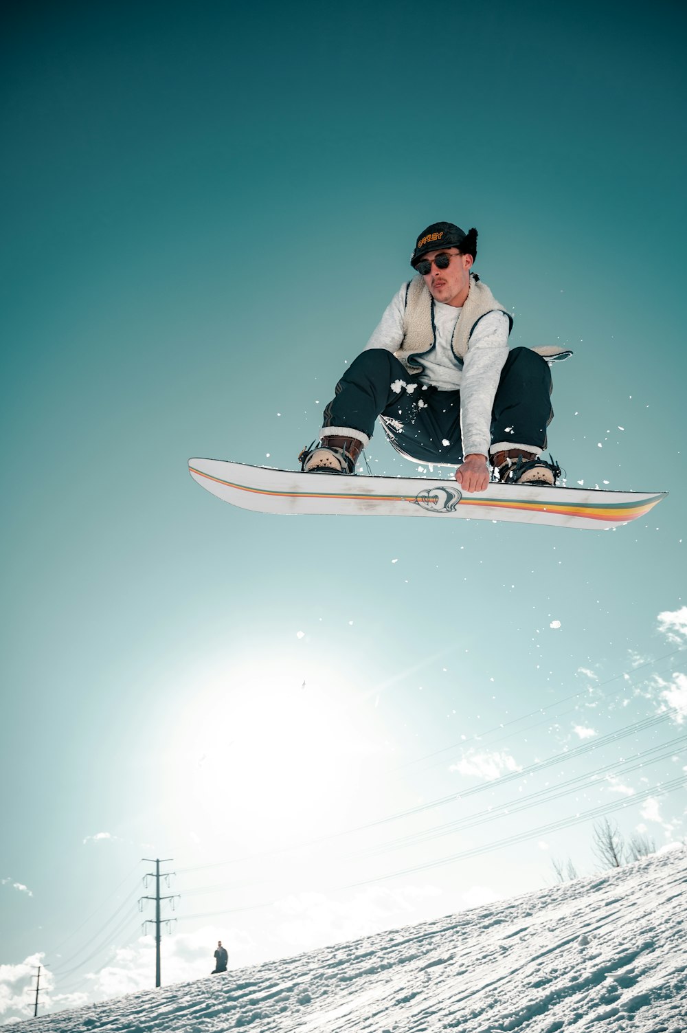 Man in een wit shirt met zwarte broek die zich vast houdt aan zijn snowboard in de lucht.