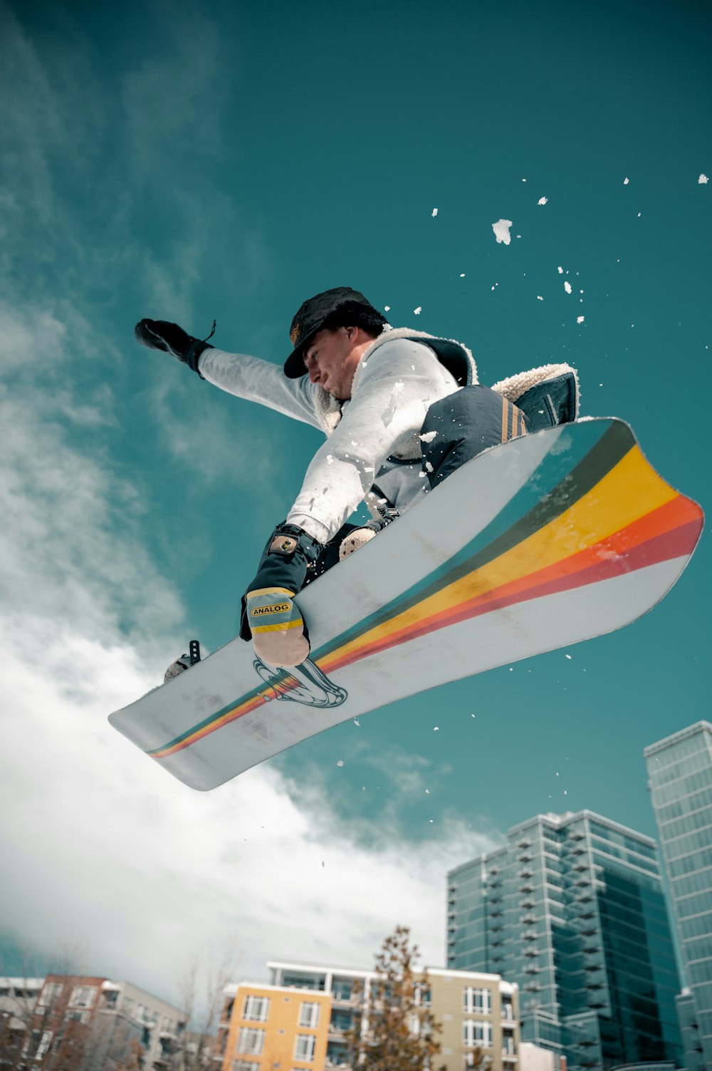 man in wit en zwart jasje die een oranje en geel snowboard rijdt 