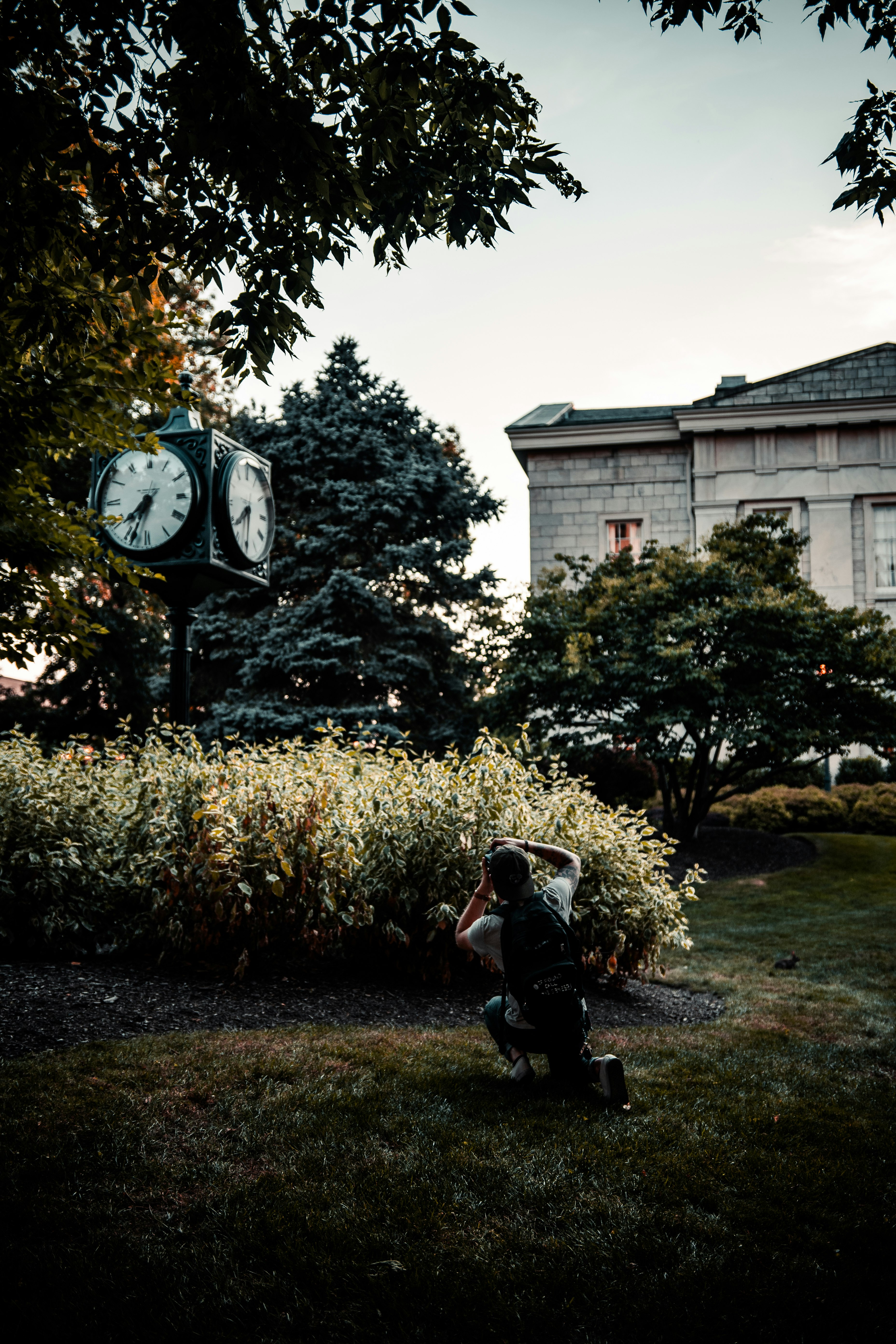 man in black jacket and black pants sitting on green grass field near white concrete building