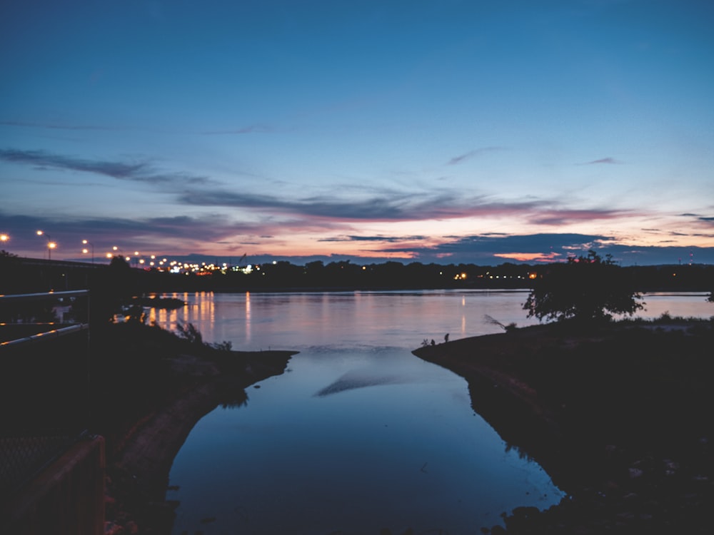 body of water near trees during sunset