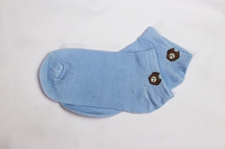 A pair of light blue socks featuring a small embroidered bear design on them. The socks are laid flat against a plain white background, showcasing their simple yet cute pattern.