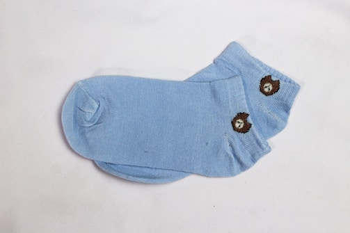 A pair of light blue socks featuring a small embroidered bear design on them. The socks are laid flat against a plain white background, showcasing their simple yet cute pattern.