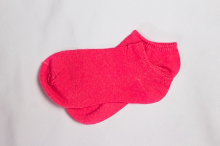 Two pink socks are neatly placed on a plain white surface. The socks have a simple design with no patterns or additional colors.