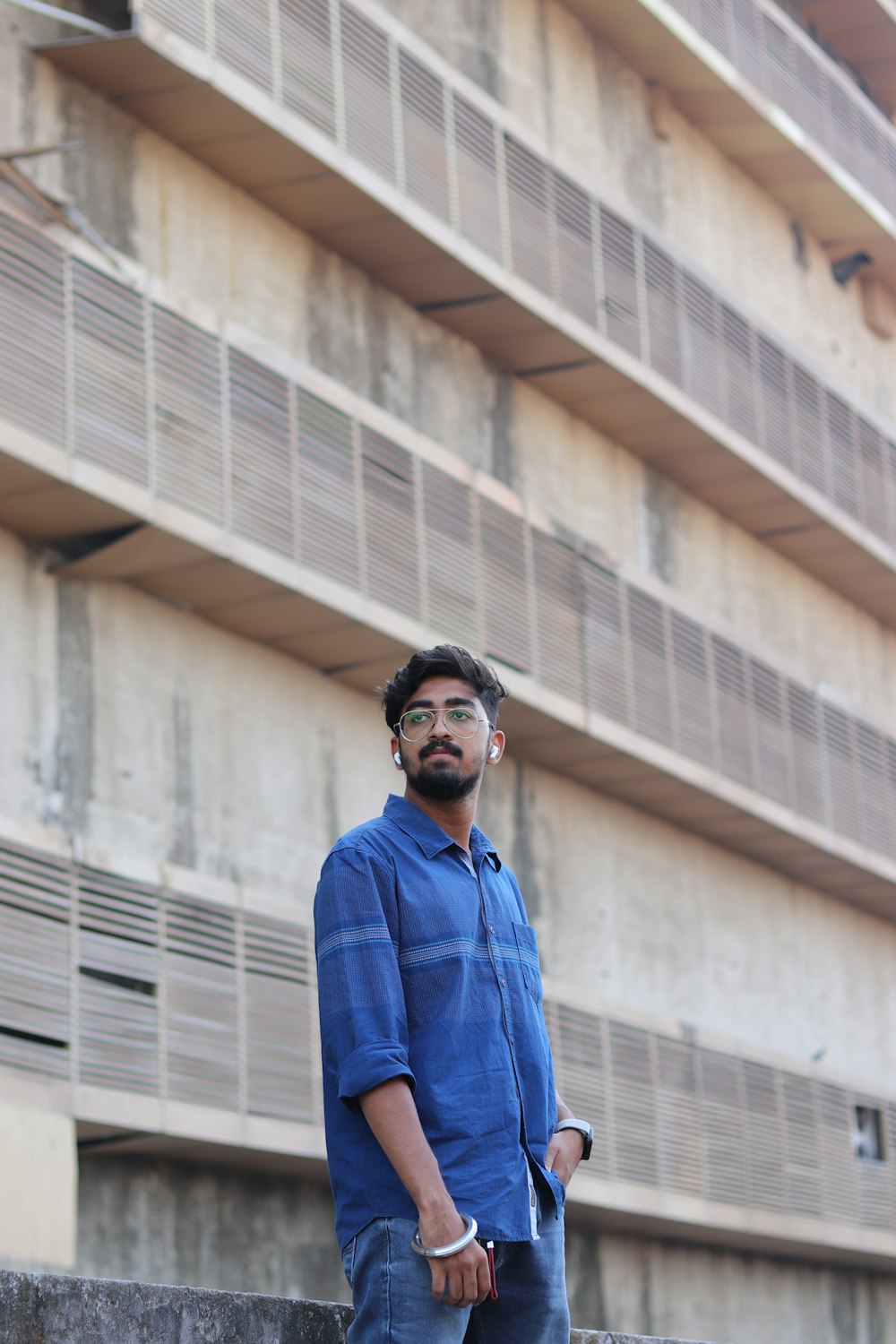 man in blue dress shirt wearing black sunglasses standing near white concrete building during daytime