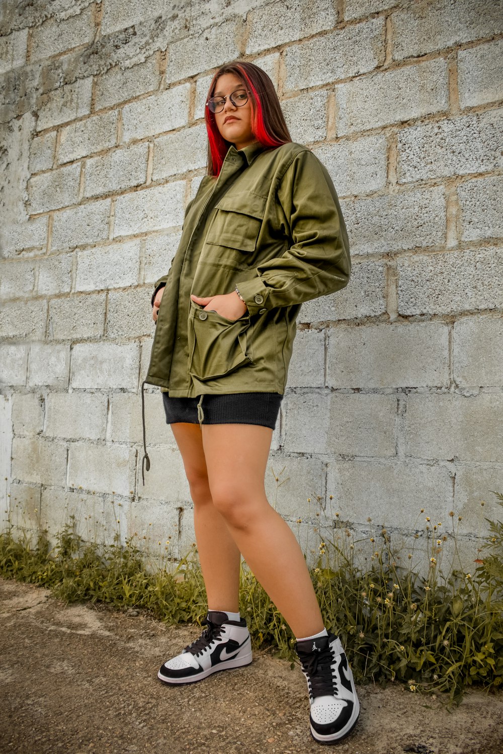 woman in green jacket and black skirt standing beside gray concrete wall