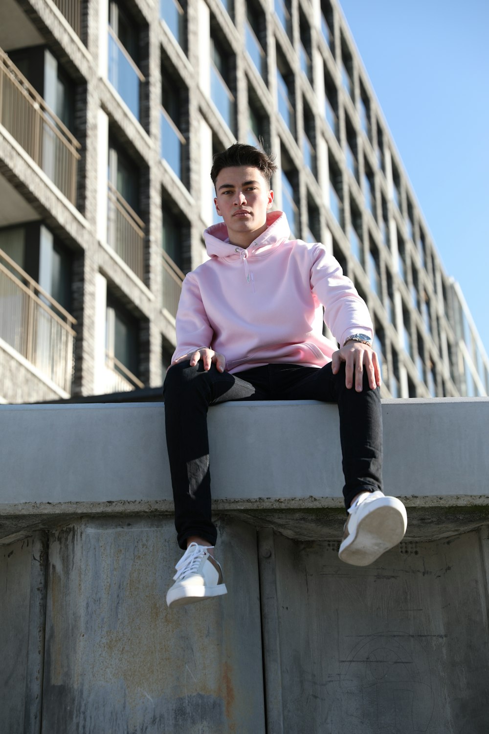 man in pink dress shirt and black pants sitting on concrete wall during daytime